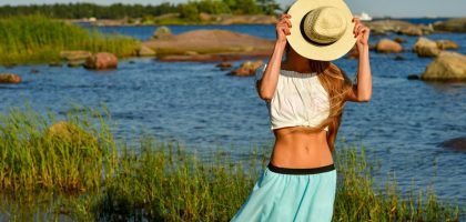 Woman enjoys a summer day by the rocky beach in Helsinki, hiding face with a straw hat