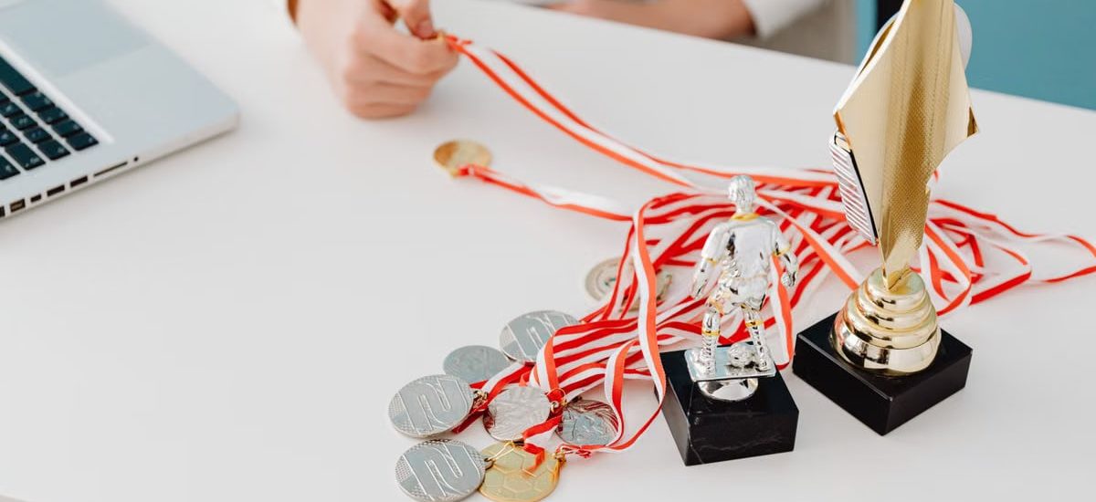 Young person displays football trophies and medals on a desk, showcasing athletic pride.